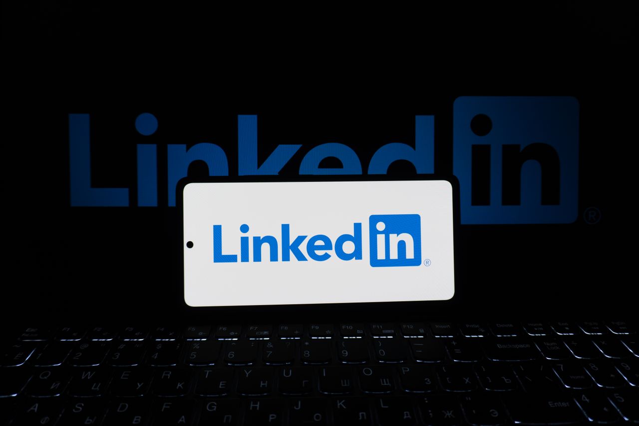 Smartphone affichant le logo LinkedIn avec un clavier et un grand logo en arrière-plan, ambiance professionnelle.
